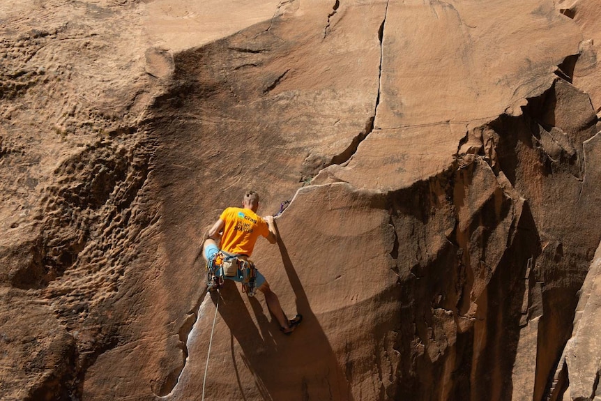 A rock climber ponders his next move while climbing the face of a big outdoor rock