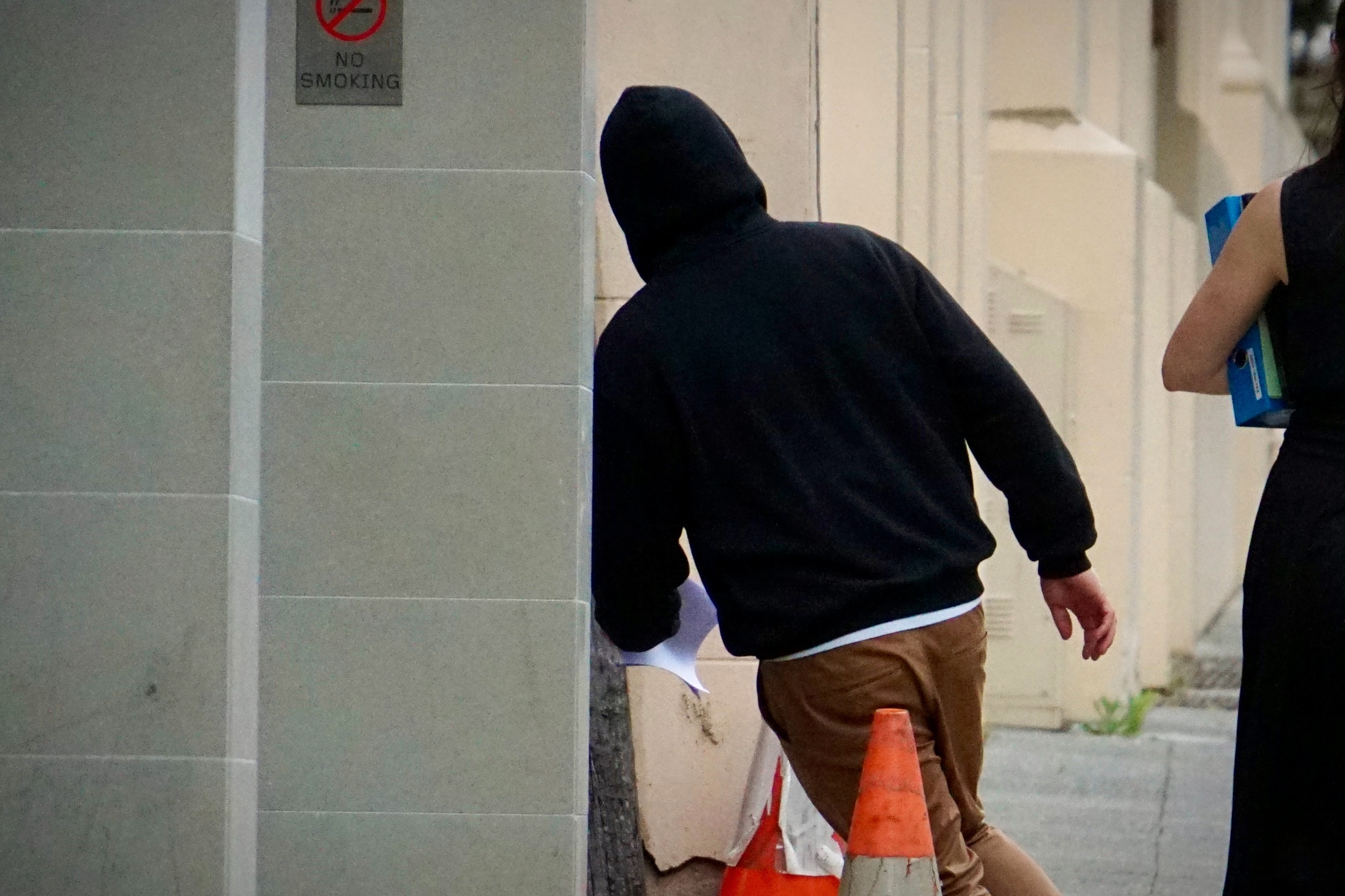A man pictured from behind in a black hooded jumper