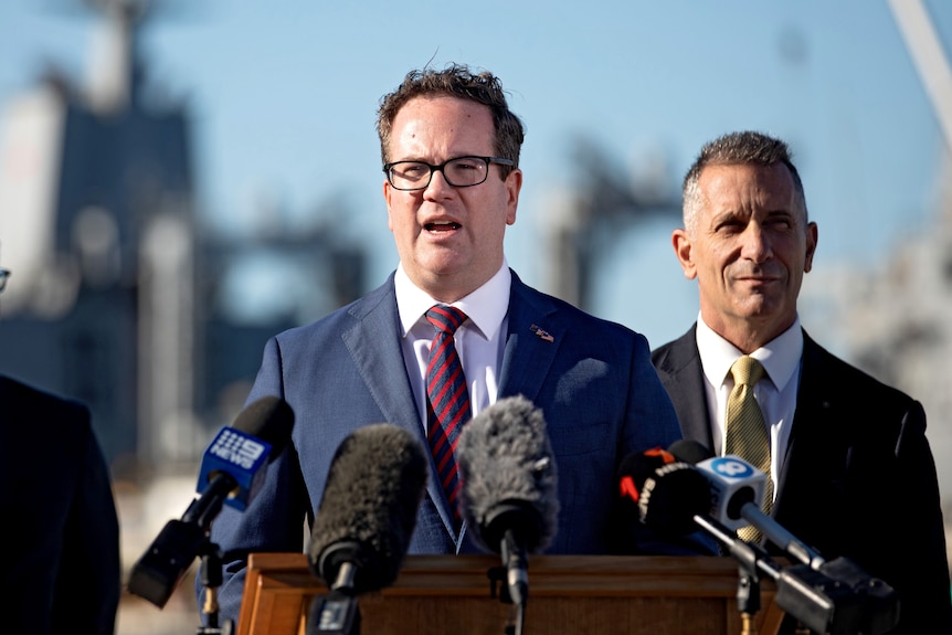 A man wearing glasses and a suit addressing a press conference