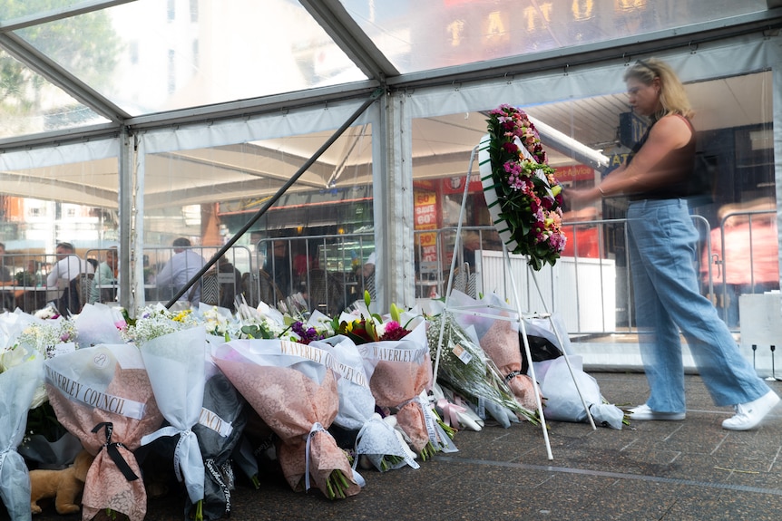 A woman lays a wreath at a memorial containing hundreds of flowers laid on the ground.