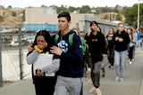 A girl cries as an older boys walks behind holding her shoulders in a line of students walking down a footpath.