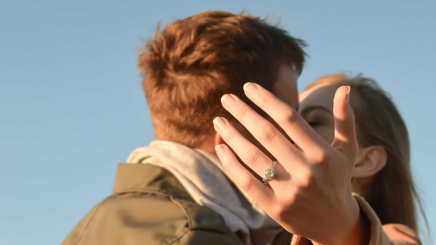 A woman's outstretched hand with an engagement ring on it.