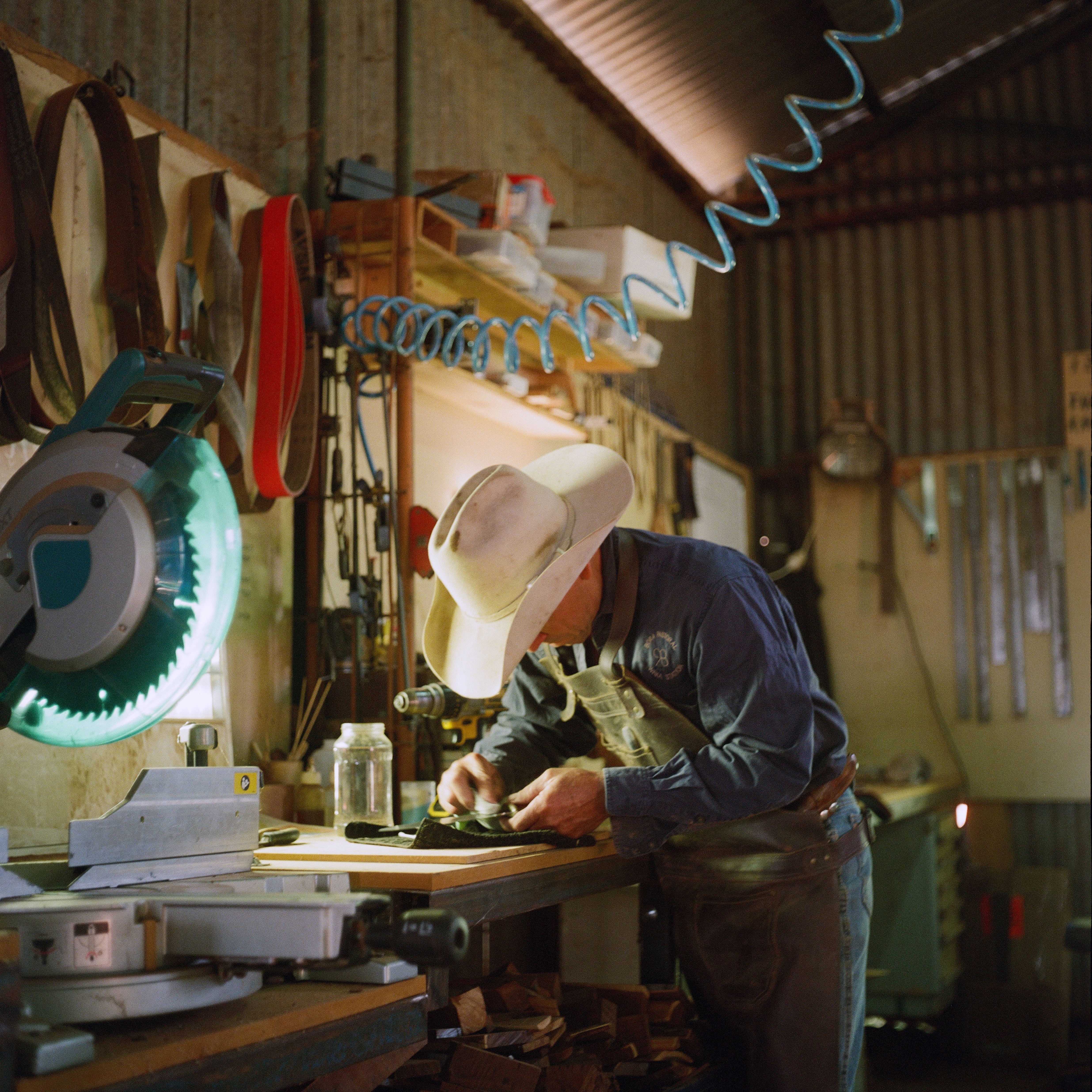 A man in a cowboy hat polishes a knife in a shed