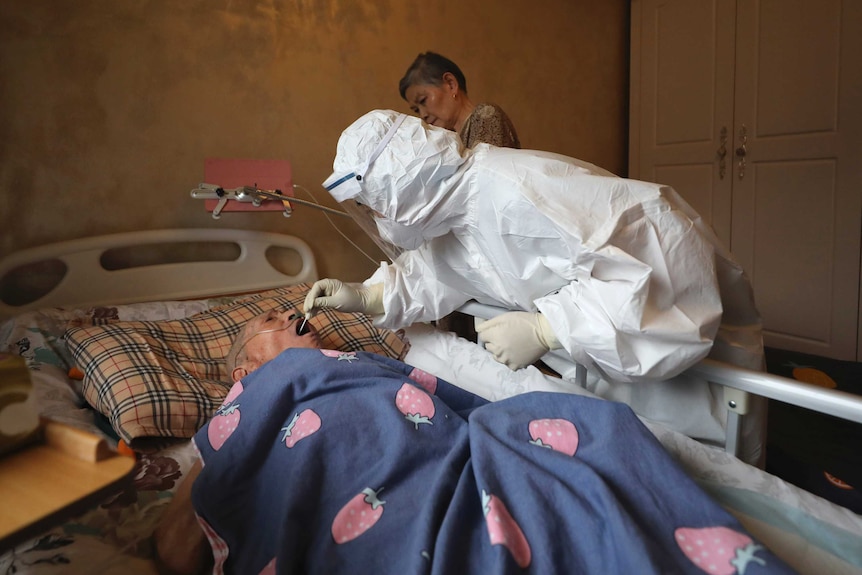 A medical worker takes a swab from a person laying in a bed.