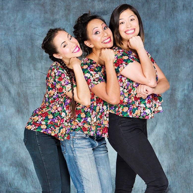 Three Asian women in matching shirts stand close together in a line, their fists on their chins