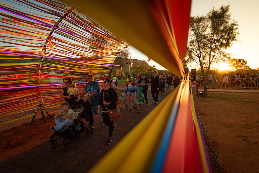 People enter Parrtjima festival under a colorful tunnel art piece.