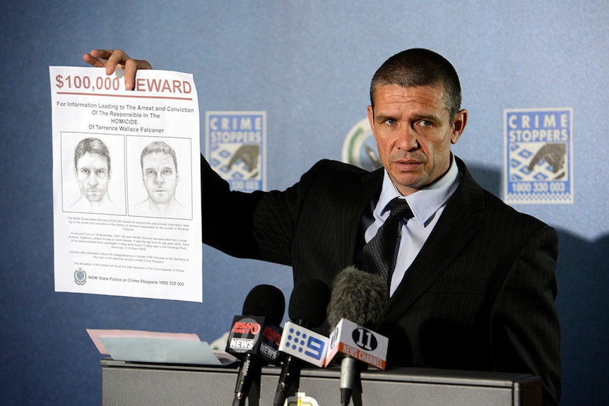 Matt Noble holds a reward notice at a press conference.