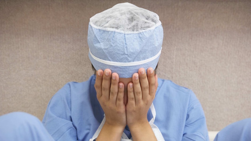 Doctor in scrubs with her head in her hands looking defeated.