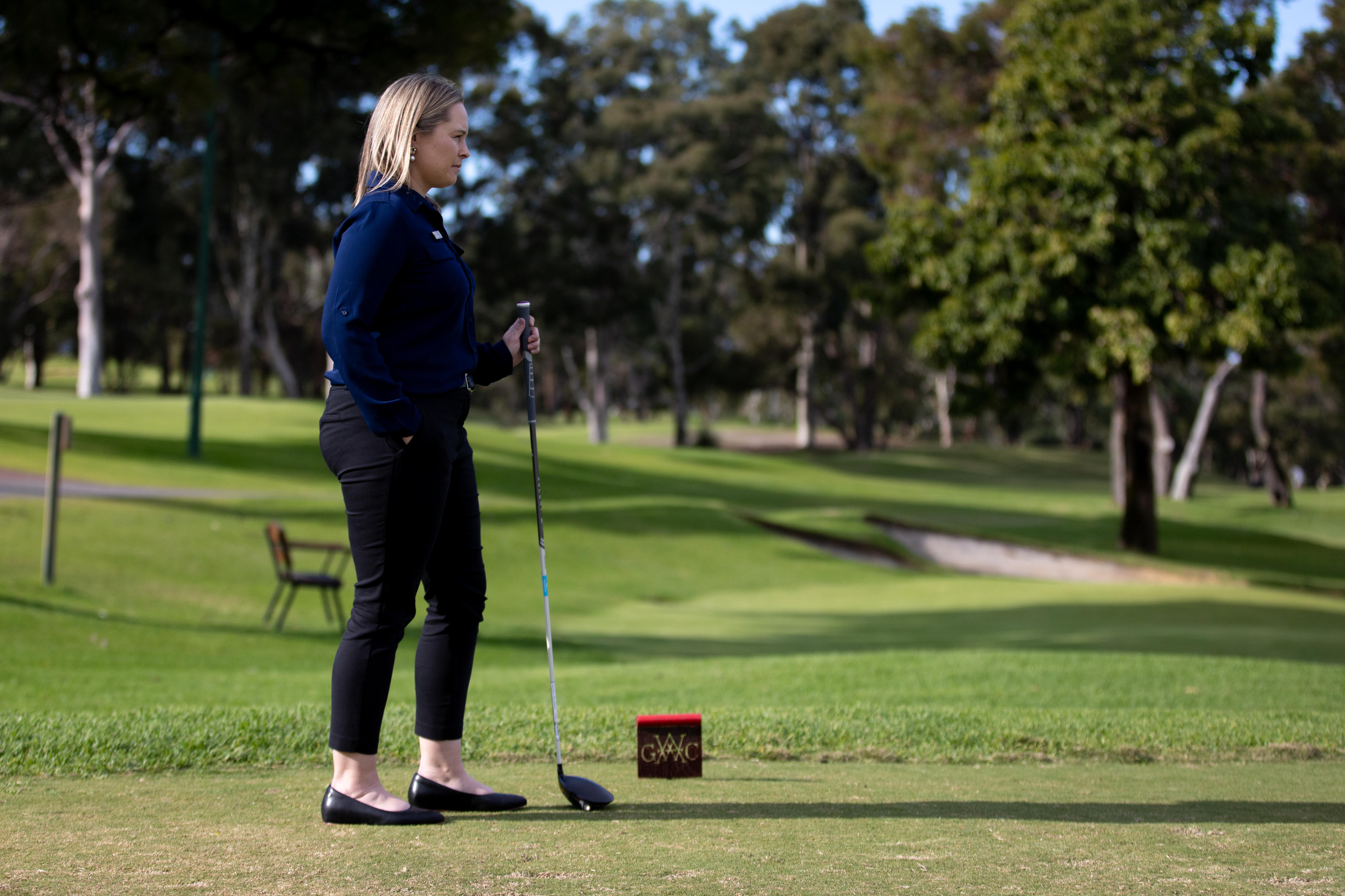 Woman holds a golf club on a well-manicured lawn.