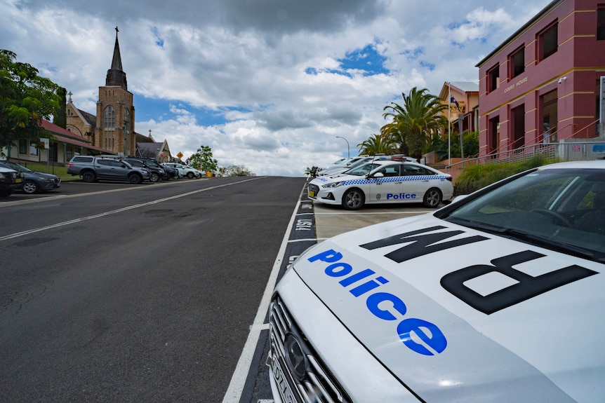 Marked police cars parked along a street with a courthouse building in the background.