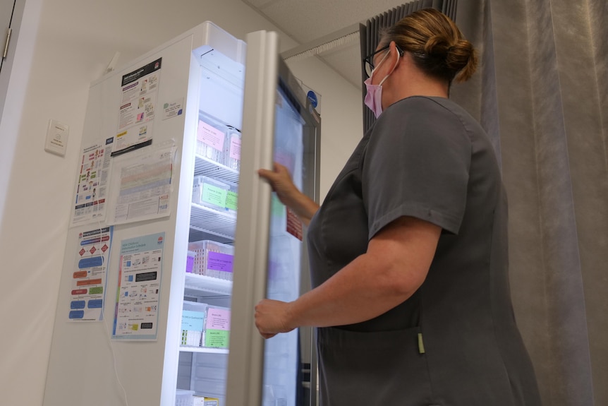 A nurse opens a door to a fridge which contains COVID vaccinations