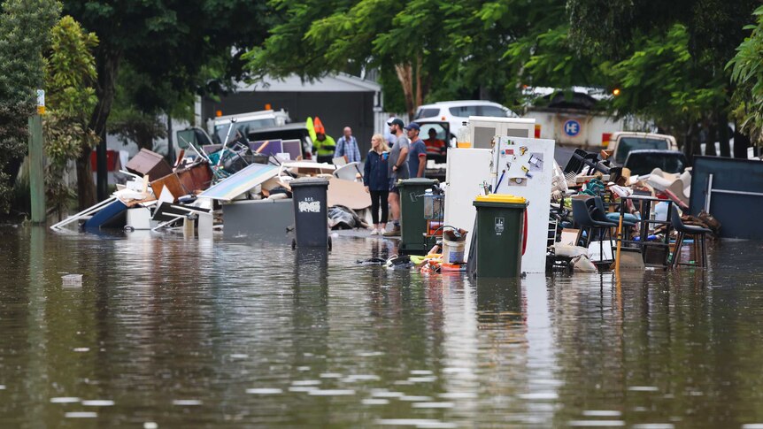 People look at rubbish in a flooded street.
