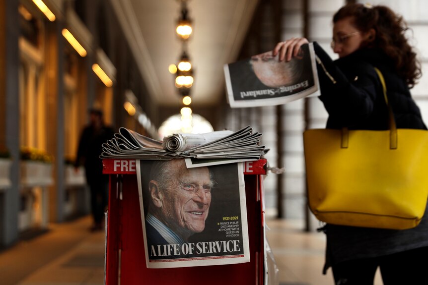A woman picks up a newspaper with a tribute to Britain's Prince Philip on the front page at Leicester Square.