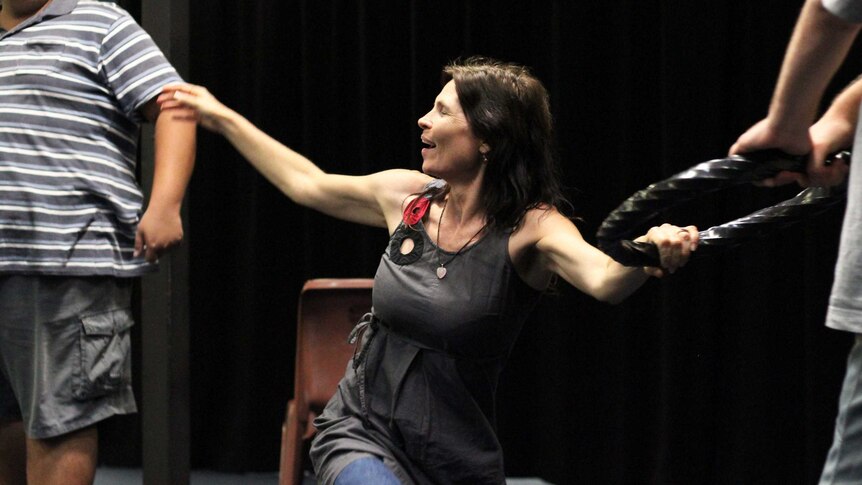 A middle-aged woman waves her hands around in a theatre space.