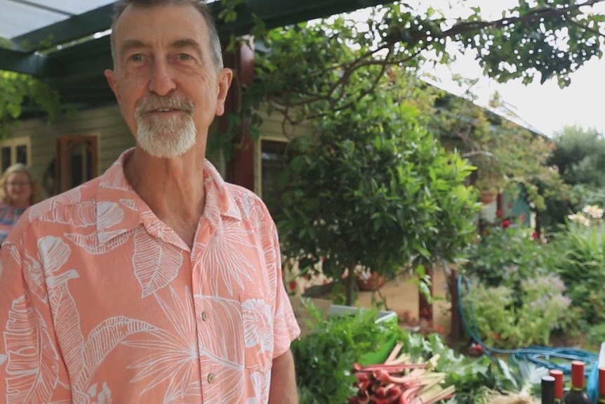 Paul McMurray stands in front of a table laden with produce in a patio in a beautiful garden.