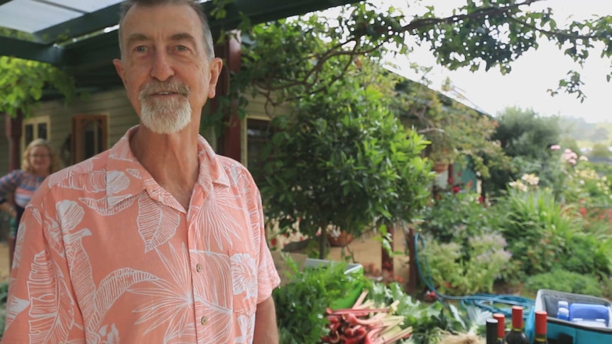 Paul McMurray stands in front of a table laden with produce in a patio in a beautiful garden.