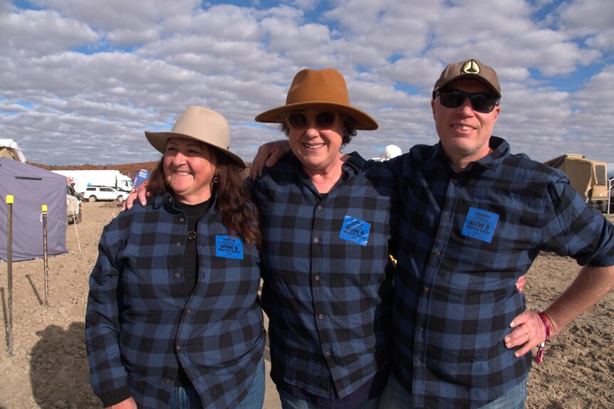 Three people standing in a campsite wearing matching blue checkered shirts. 