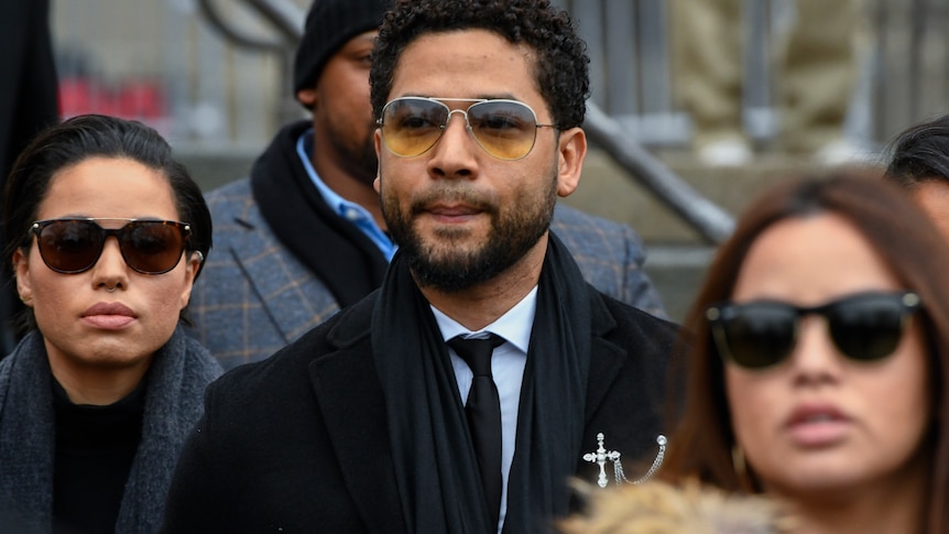 Jussie Smollett wearing sunglasses and surrounded by others also in sunglasses