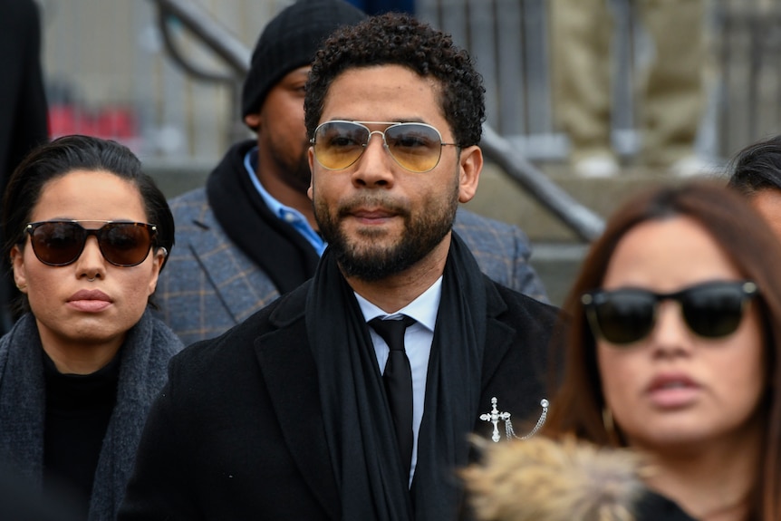 Jussie Smollett wearing sunglasses and surrounded by others also in sunglasses
