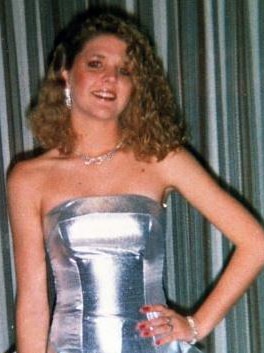 A young woman wearing a silver strapless ball dress and jewellery smiles for the camera with her hand on her hip.