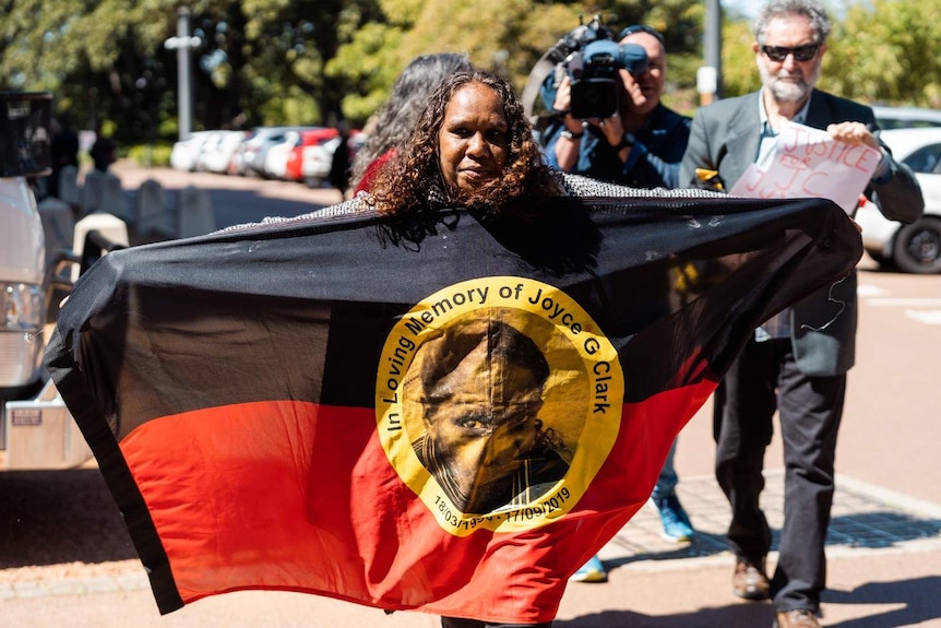 JCs sister Bernadette holding an Aboriginal flag with JC's face in the centre