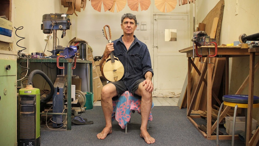 Richard Morgan sitting in his cream-coloured studio, with his guitar making instruments surrounding him.