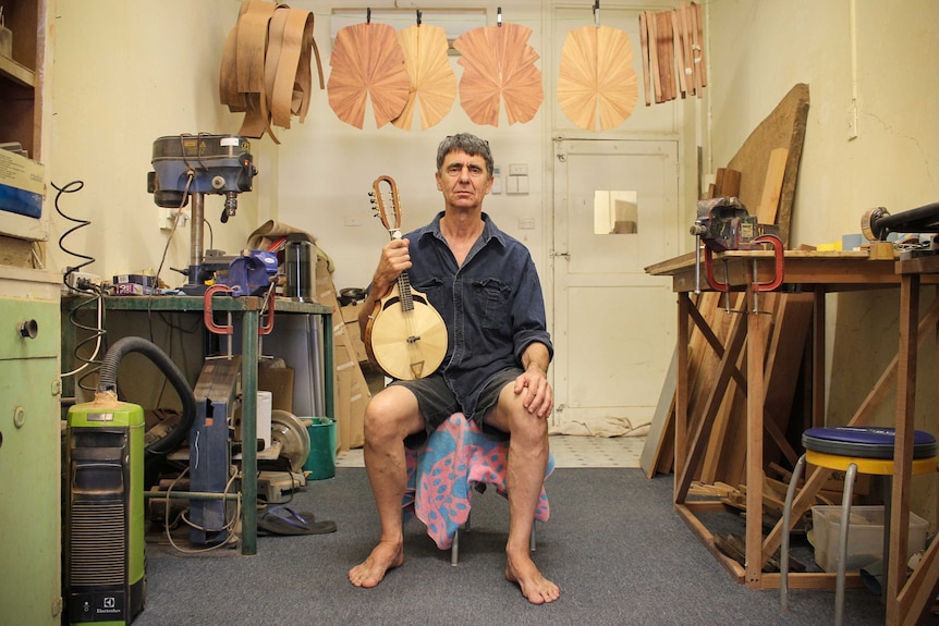 Richard Morgan sitting in his cream-coloured studio, with his guitar making instruments surrounding him.