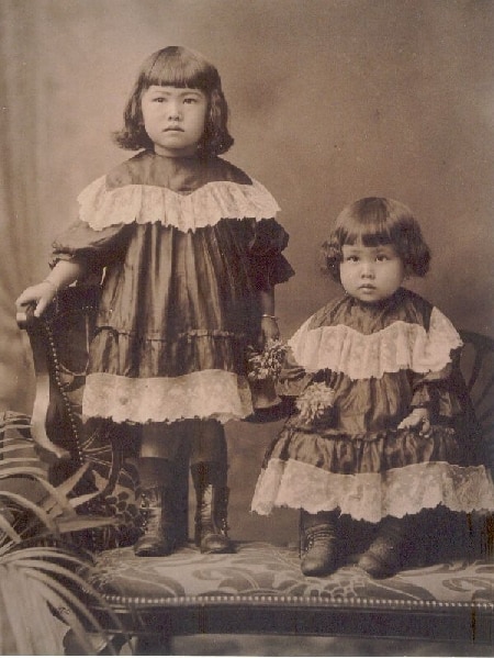 Two young girls in frilly dresses in an old photograph