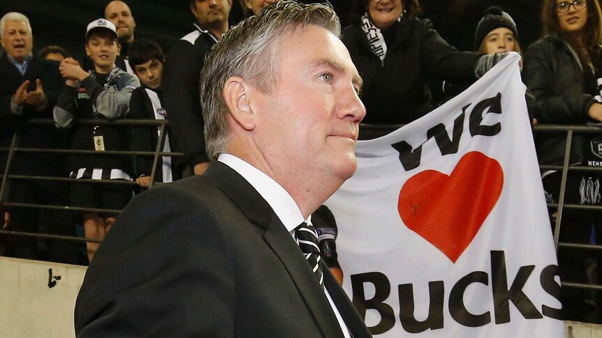 Eddie McGuire walks past Collingwood fans holding up a sign saying We Love Bucks