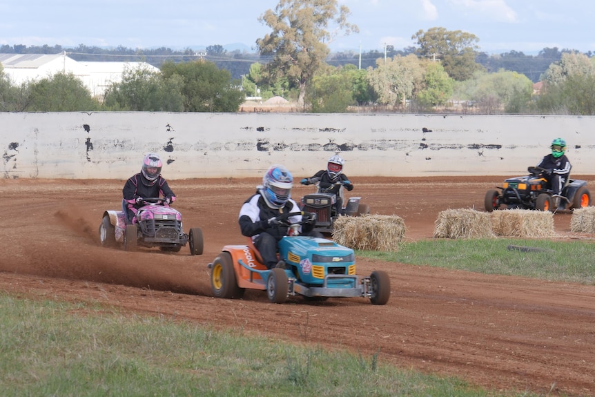 Four people riding lawn mowers on a dirt track 