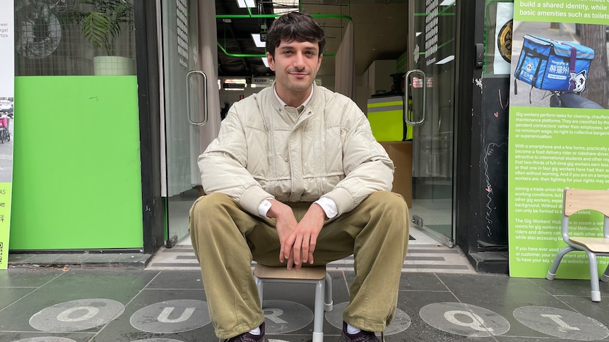 Andrew Copolov sits on small chair outside shop doors on the street