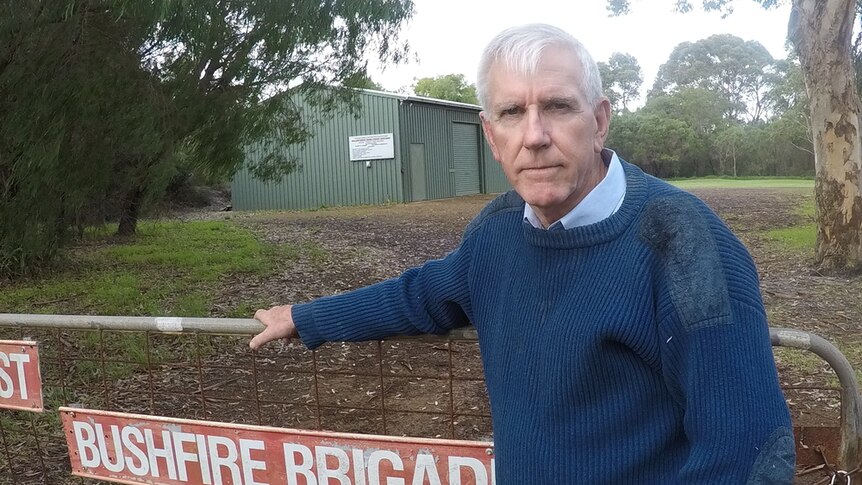 A volunteer firefighter stands at the front gate of a bushfire station.