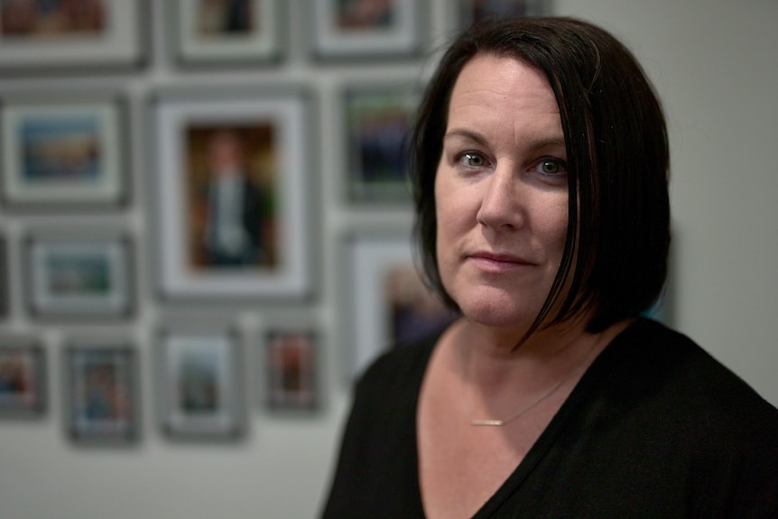 A woman stands in front of a wall of photos of her son.