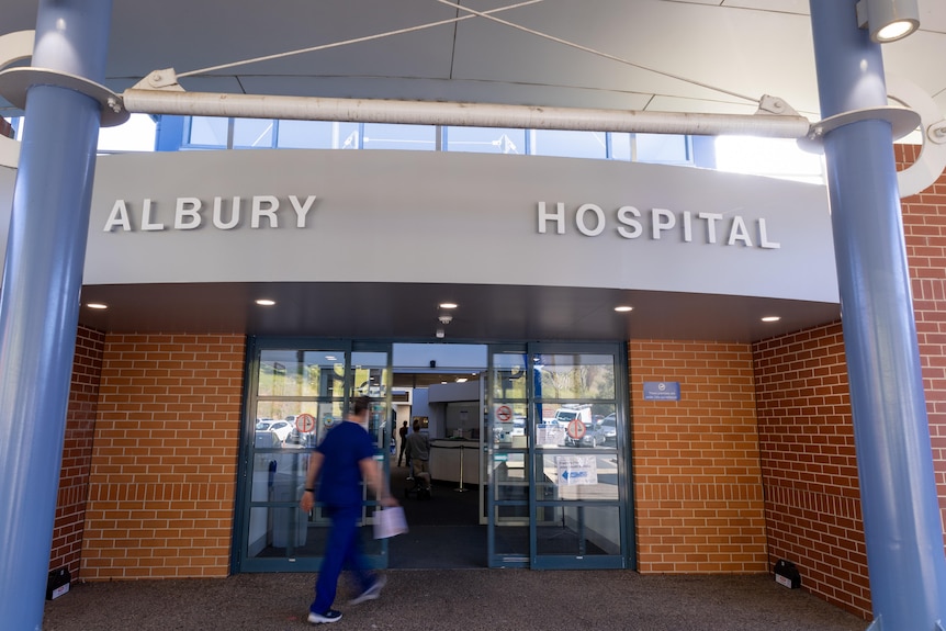 A person in blue medical scrubs walks through the automatic doors and into the Albury hospital