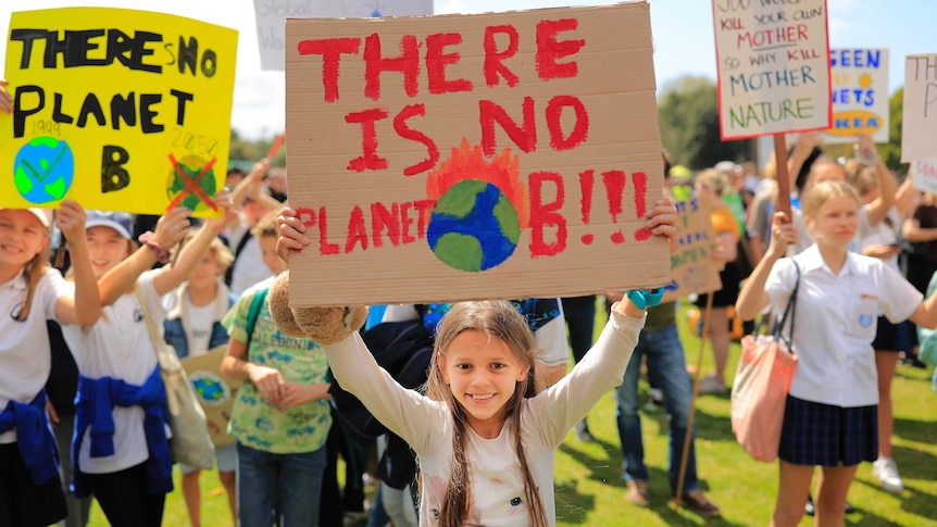 young girl holding a han-made sign saying 'there is no planet B' amongst other children holding signs