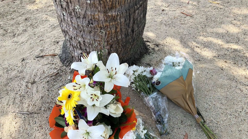 A bunch of flowers laid on the sand at a swimming lagoon.