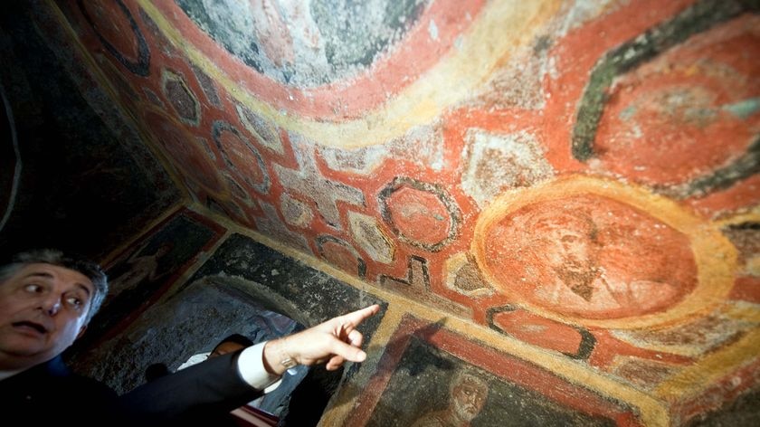 An archaeologist gestures towards a watercolour of St Paul at the 'Cubicle of Apostles'