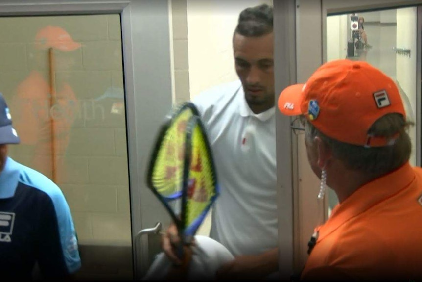 Kyrgios walks through a door from a hallway with two broken racquets in his hand. A linesman and security guard watch on