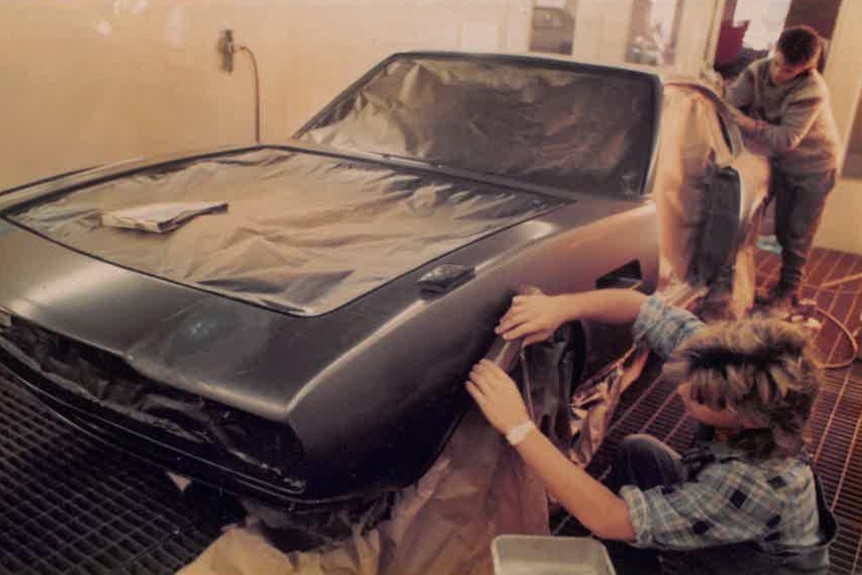 Two young men work on the body of a car, restoring the paint