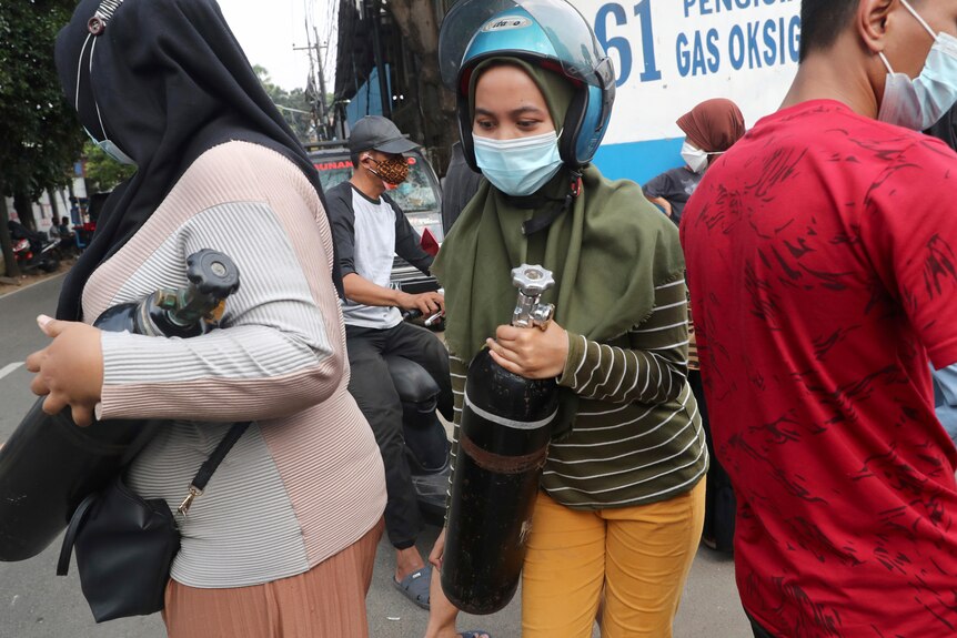 A woman carries her oxygen tank after having it refilled at a recharging station