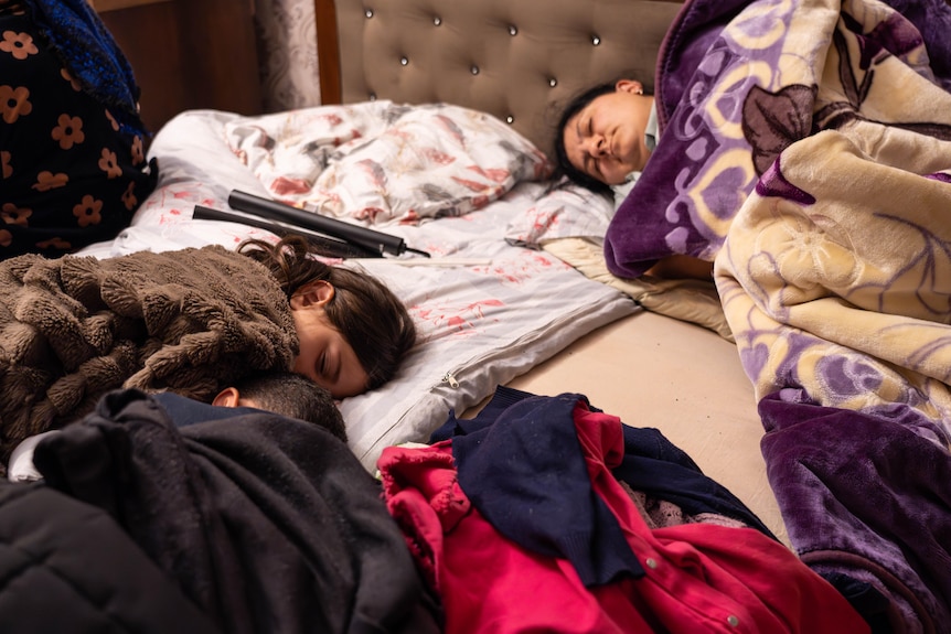 Two refugees sleep with blankets on a bed.