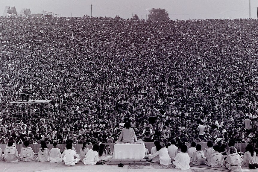 A sea of people sitting front of a stage in a black and white photo