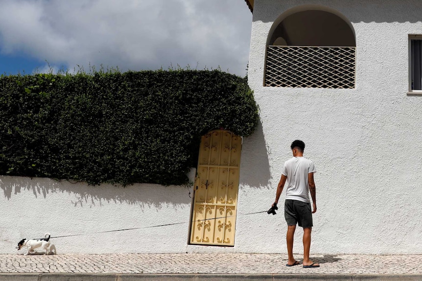 Man walks dog next to white apartment building