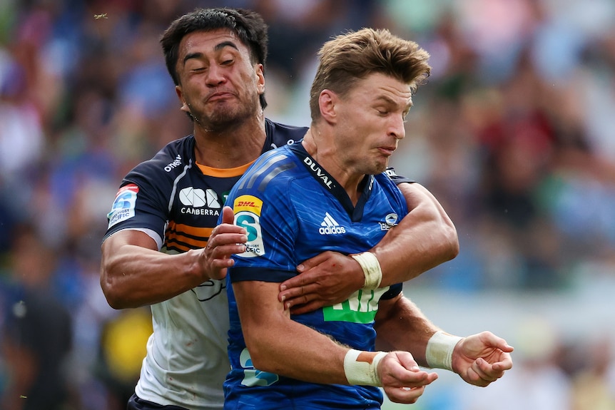 A Blues player is tackled by a Brumbies opponent.