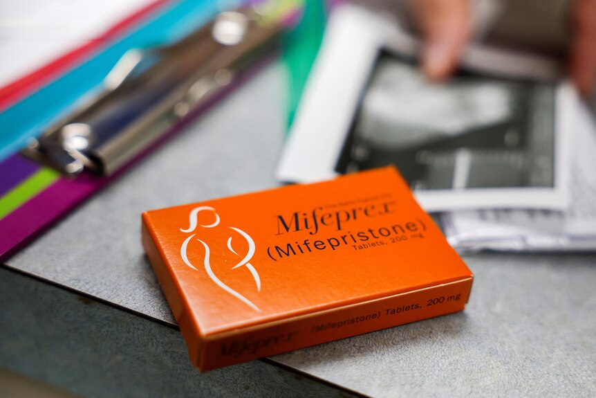 An orange cardboard box labelled Mifepristone sits on a desk near clipboards and blurred out papers