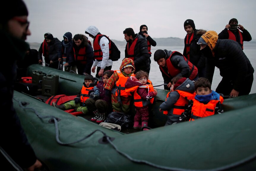 Migrants including small children wearing life jackets on a grey rubber dingy. 