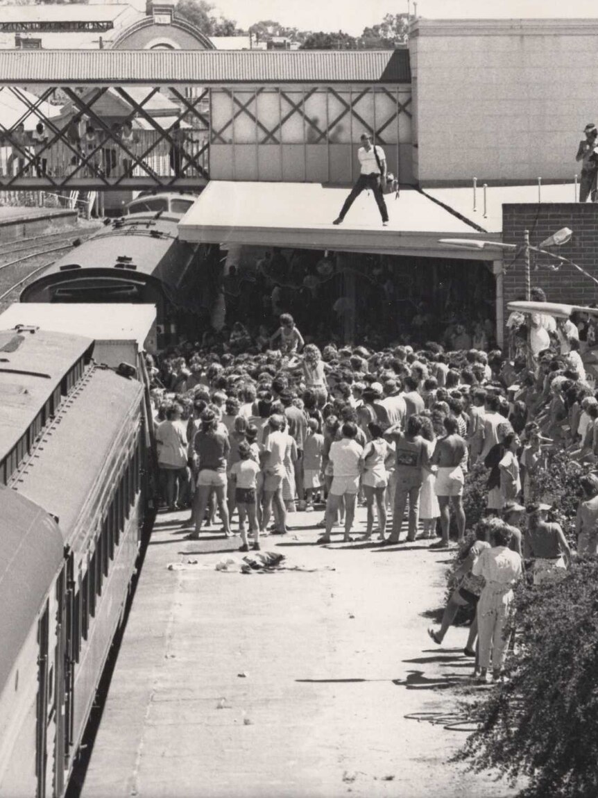 A large crowd of people at a train station, where a band has arrived to perform.