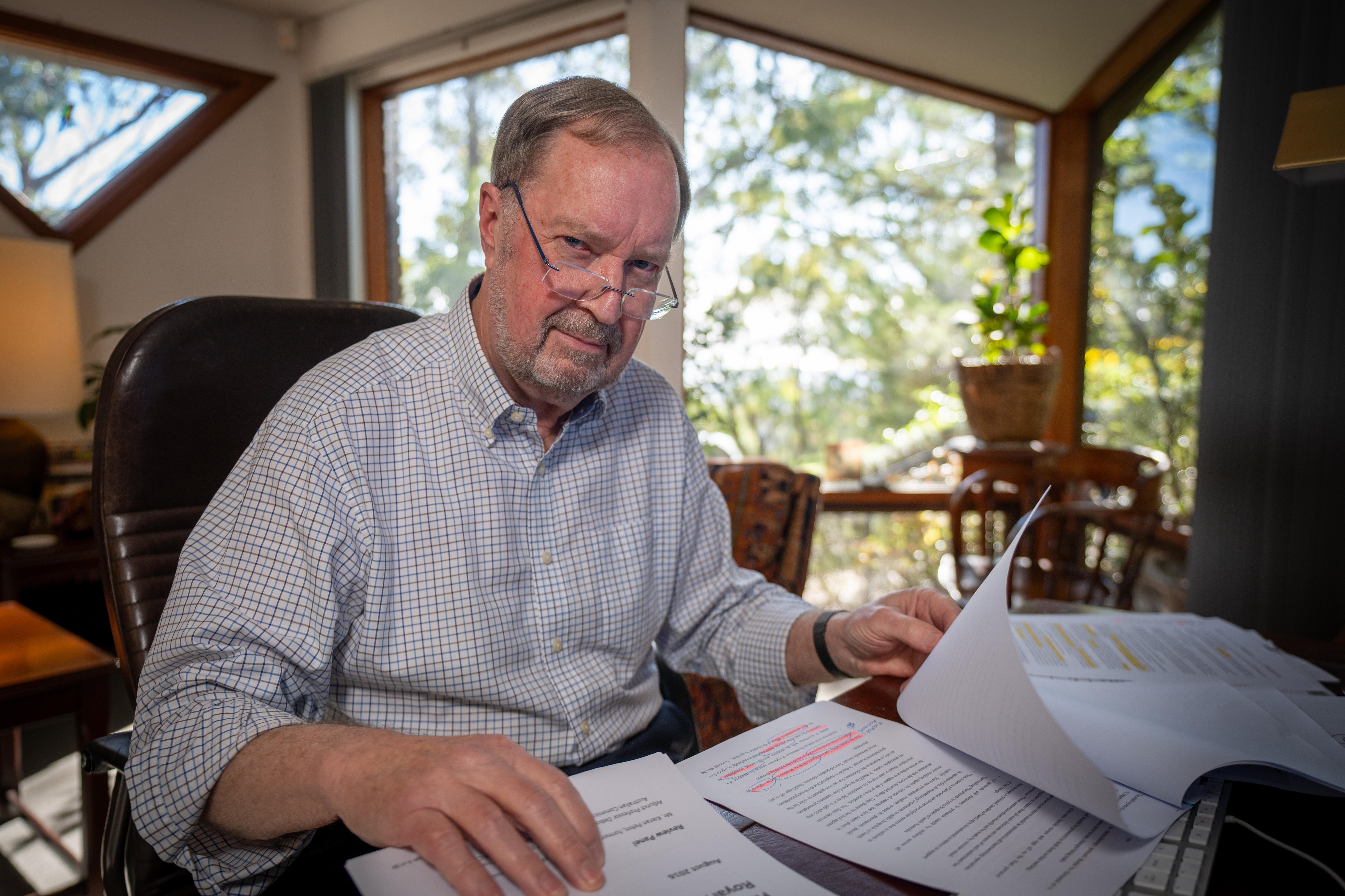 A man wearing glasses flicking through papers looking at the camera. 