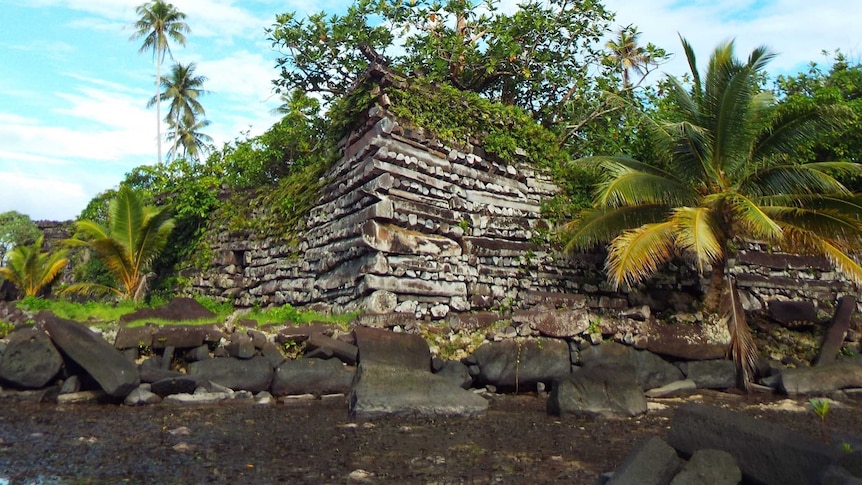 A ruined stone structure sits on a bank behind shallow water.