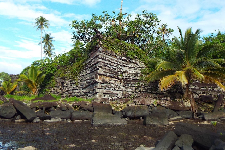 A ruined stone structure sits on a bank behind shallow water.